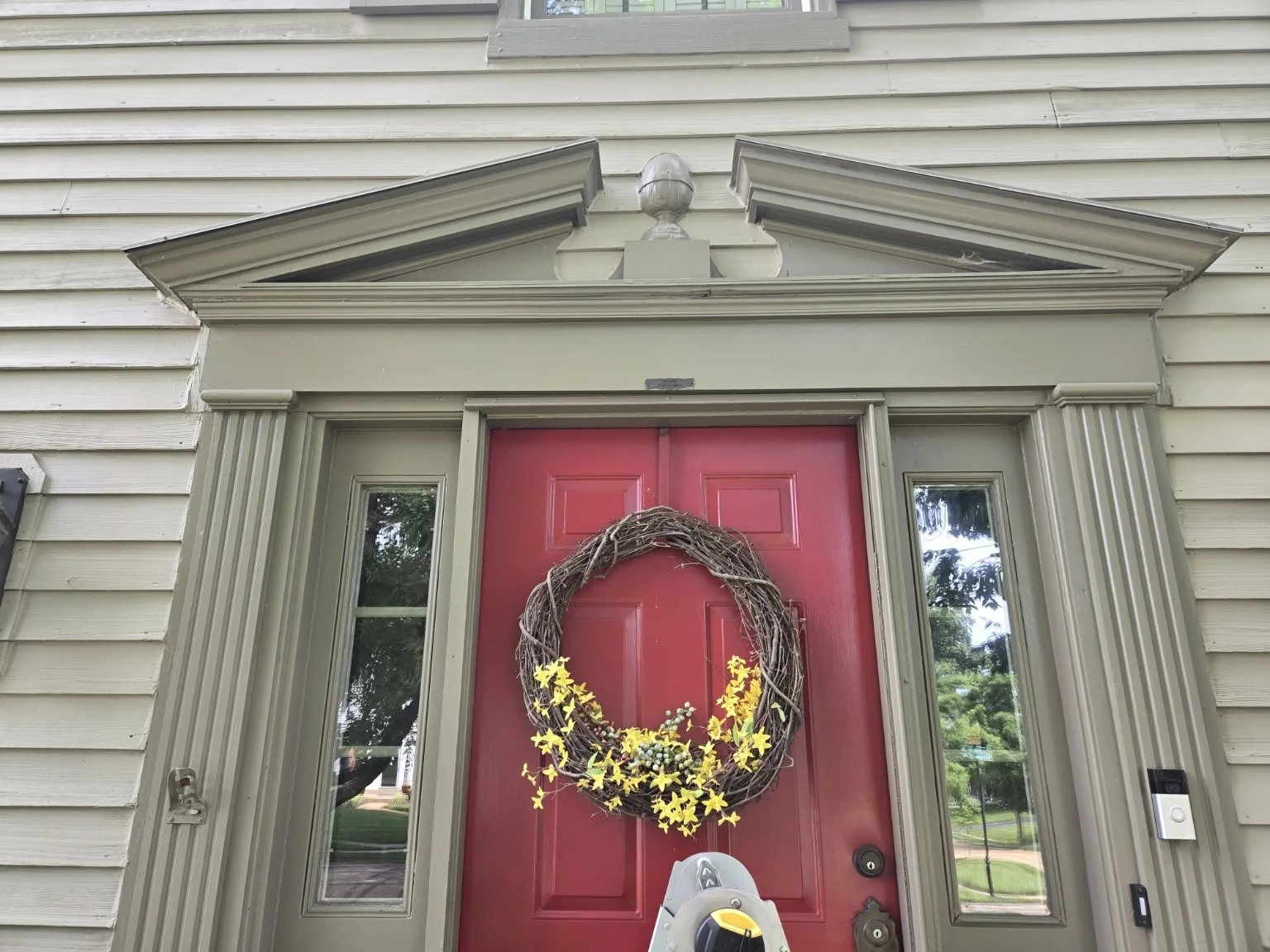 Original deteriorated architectural pediment above a red front door